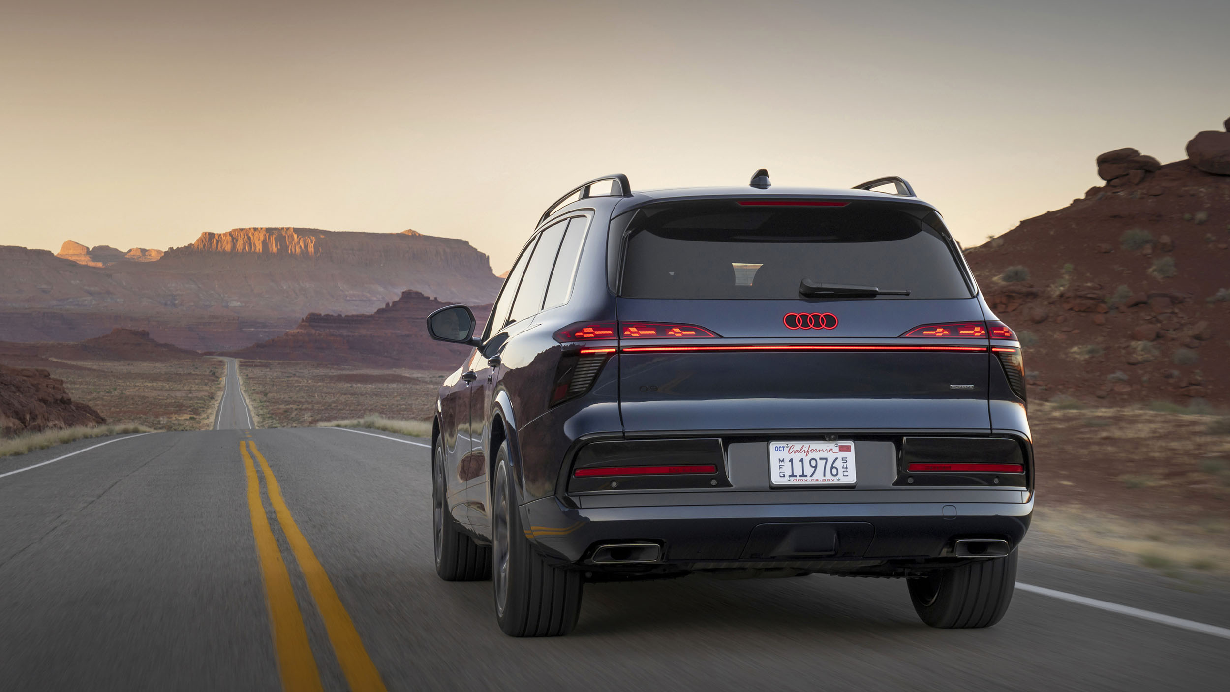 Ein blauer Audi Q9 fährt auf einer Straße durch die Wüste.