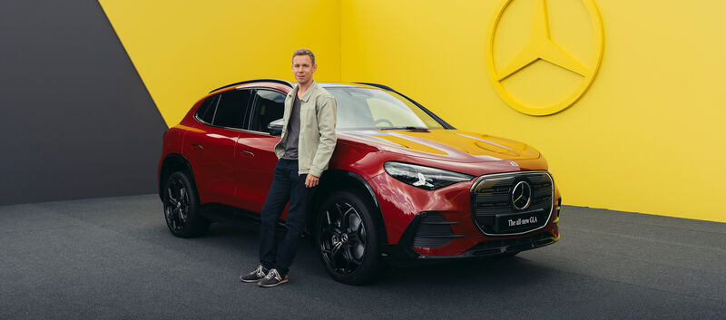Ein Mann lehnt an einem roten Mercedes-SUV.