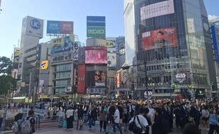 Das Bild zeigt Shibuya Crossing bei tag mit vielen Menschen und Hochhäusern