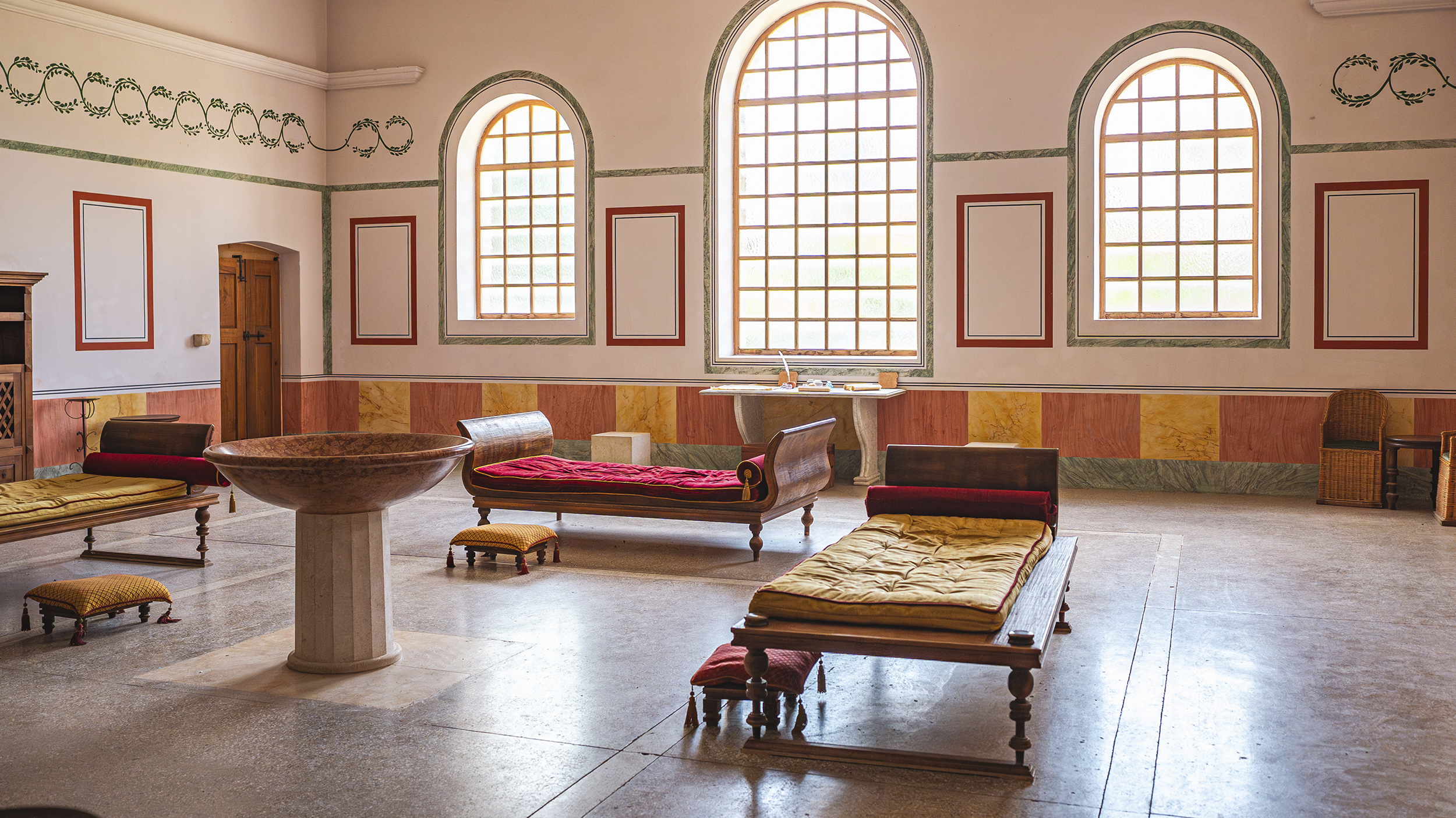 Innenansicht Therme in Carnuntum. 3 große Fenster, mehrere Liegen, antike Einrichtung.