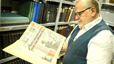 ÖAMTC-Archivar Joachim Moser, trägt ein weißes Kurzarmhemd mit Pullunder. Er blättert in einen Buch aus dem Archiv.