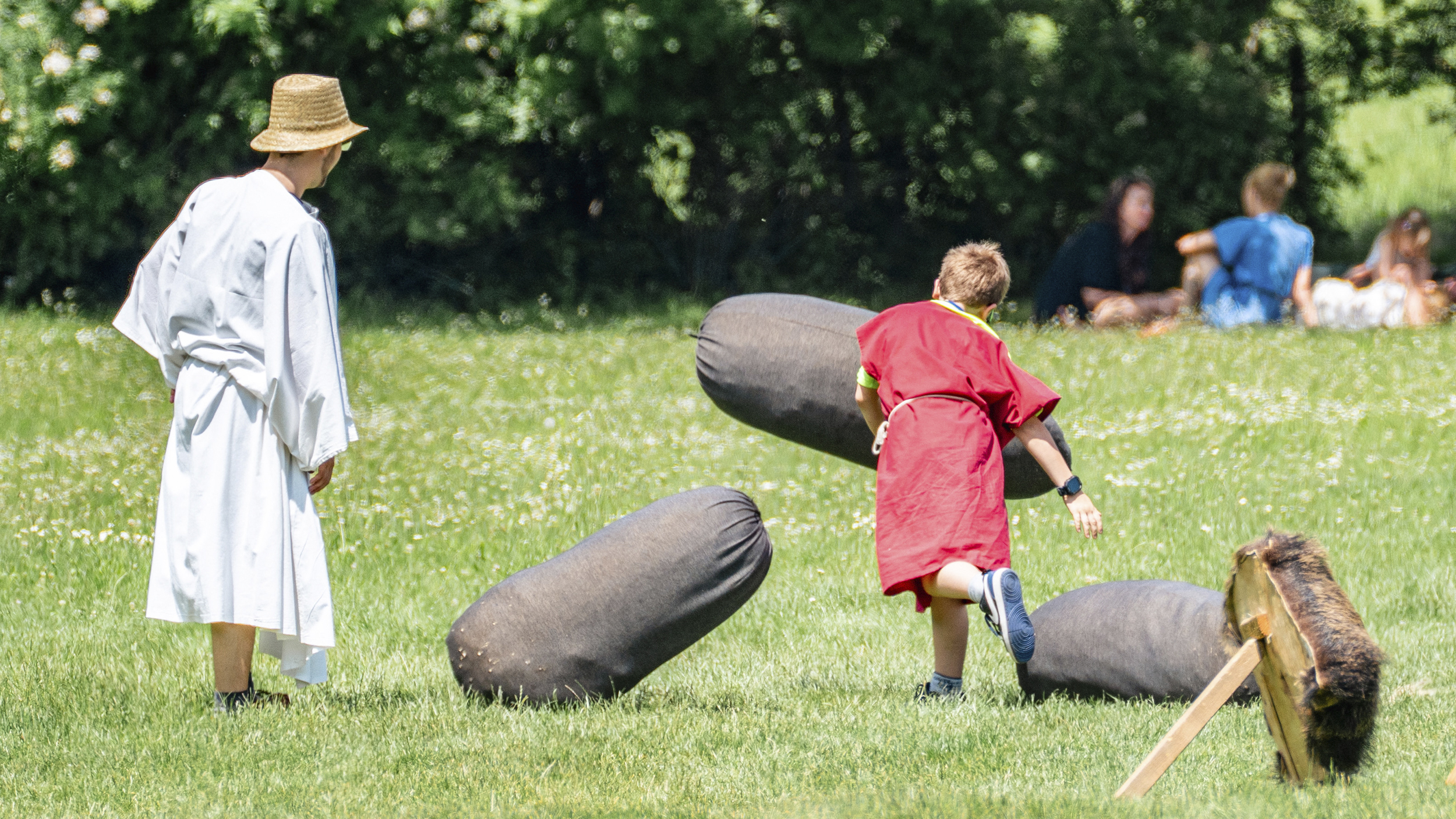 Kinder spielen in altrömischen Gewand auf einer Wiese mit Säcken.