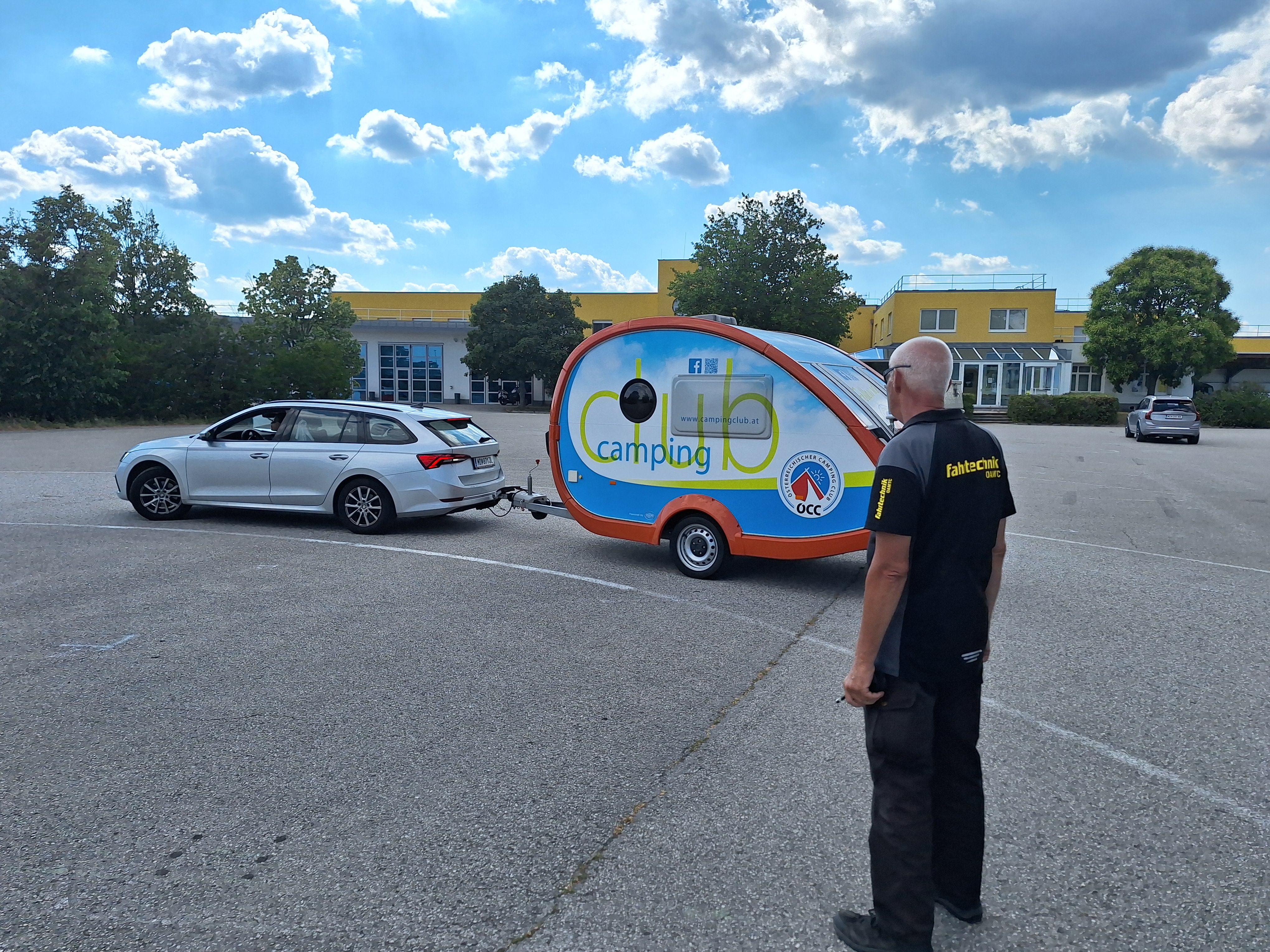 Es ist ein Mann von der Seite zu sehen. Er schaut auf ein silbernes Auto mit Camping-Anhänger.