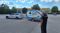 Es ist ein Mann von der Seite zu sehen. Er schaut auf ein silbernes Auto mit Camping-Anhänger.