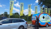 Man sieht zwei Männer, die vor der Anhängerkupplung eines Autos stehen und miteinader sprechen.