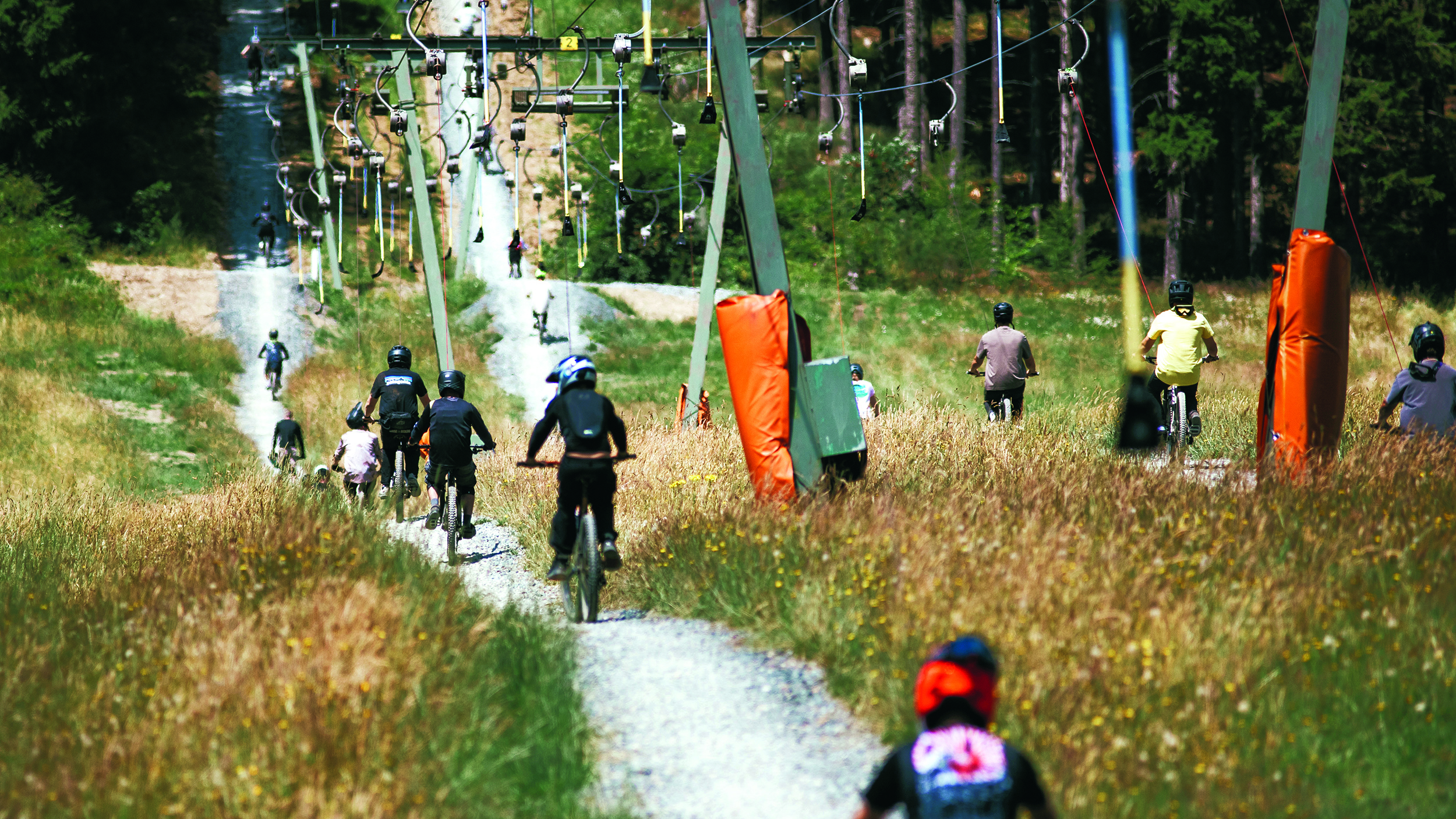 Mountainbiker:innen fahren neben einem Schlepplift einen sommerlichen Berghang hinauf.