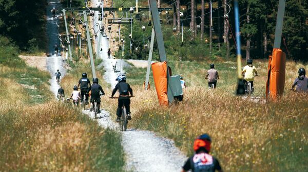 Mountainbiker:innen fahren neben einem Schlepplift einen sommerlichen Berghang hinauf.