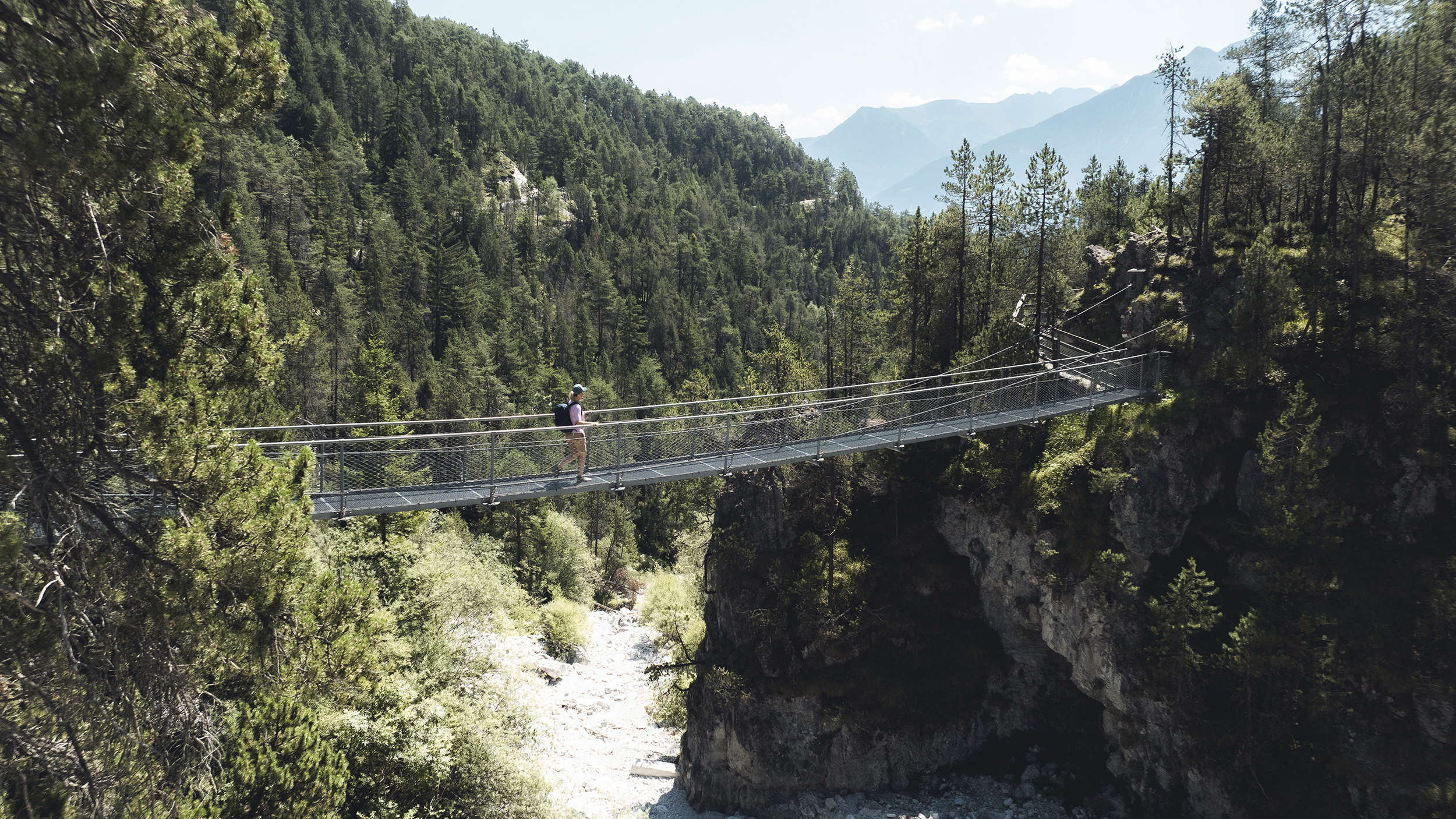 Eine Wanderin geht über eine Hängebrücke, die über eine Schlucht führt.