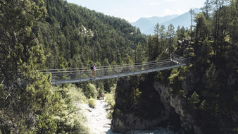Eine Wanderin geht über eine Hängebrücke, die über eine Schlucht führt.