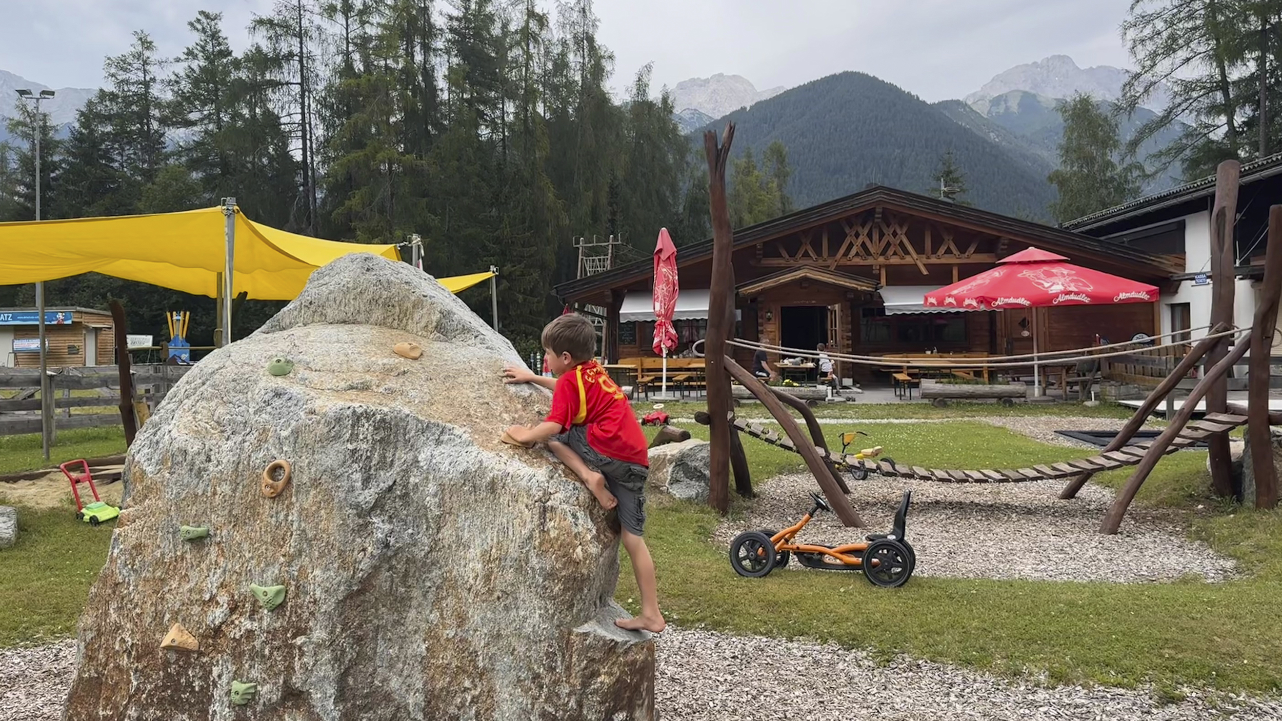 Ein Bub klettert am Spielplatz auf einen Stein mit Bouldergriffen.