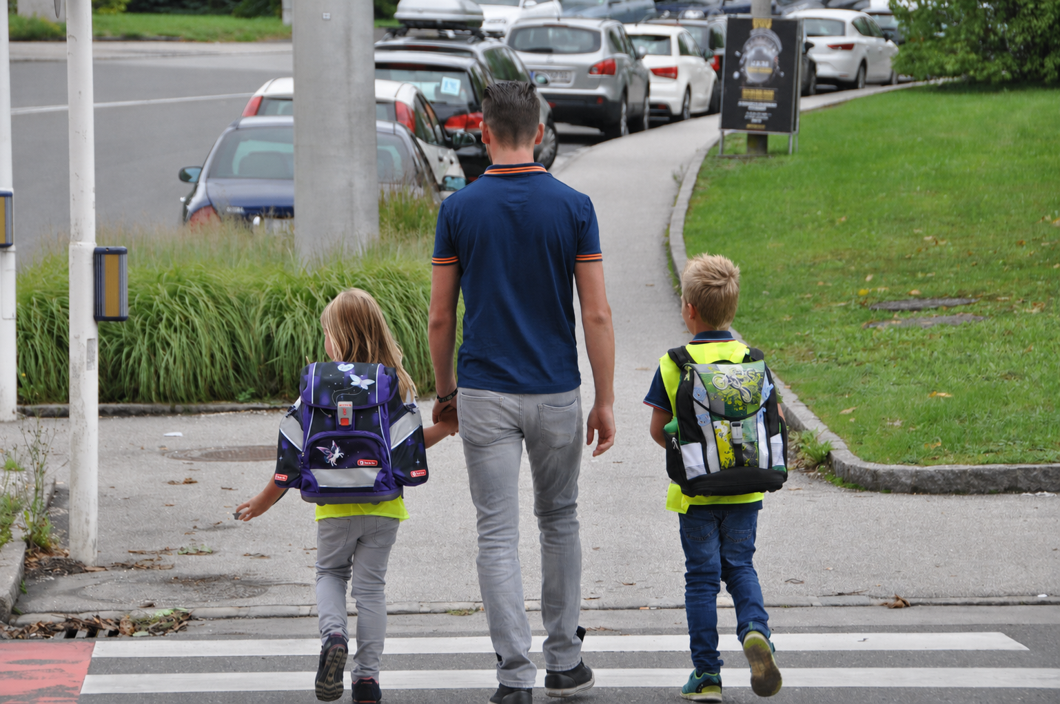 Eine erwachsene Person geht mit zwei Schulkindern über den Zebrastreifen.