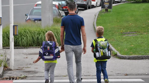 Eine erwachsene Person geht mit zwei Schulkindern über den Zebrastreifen.