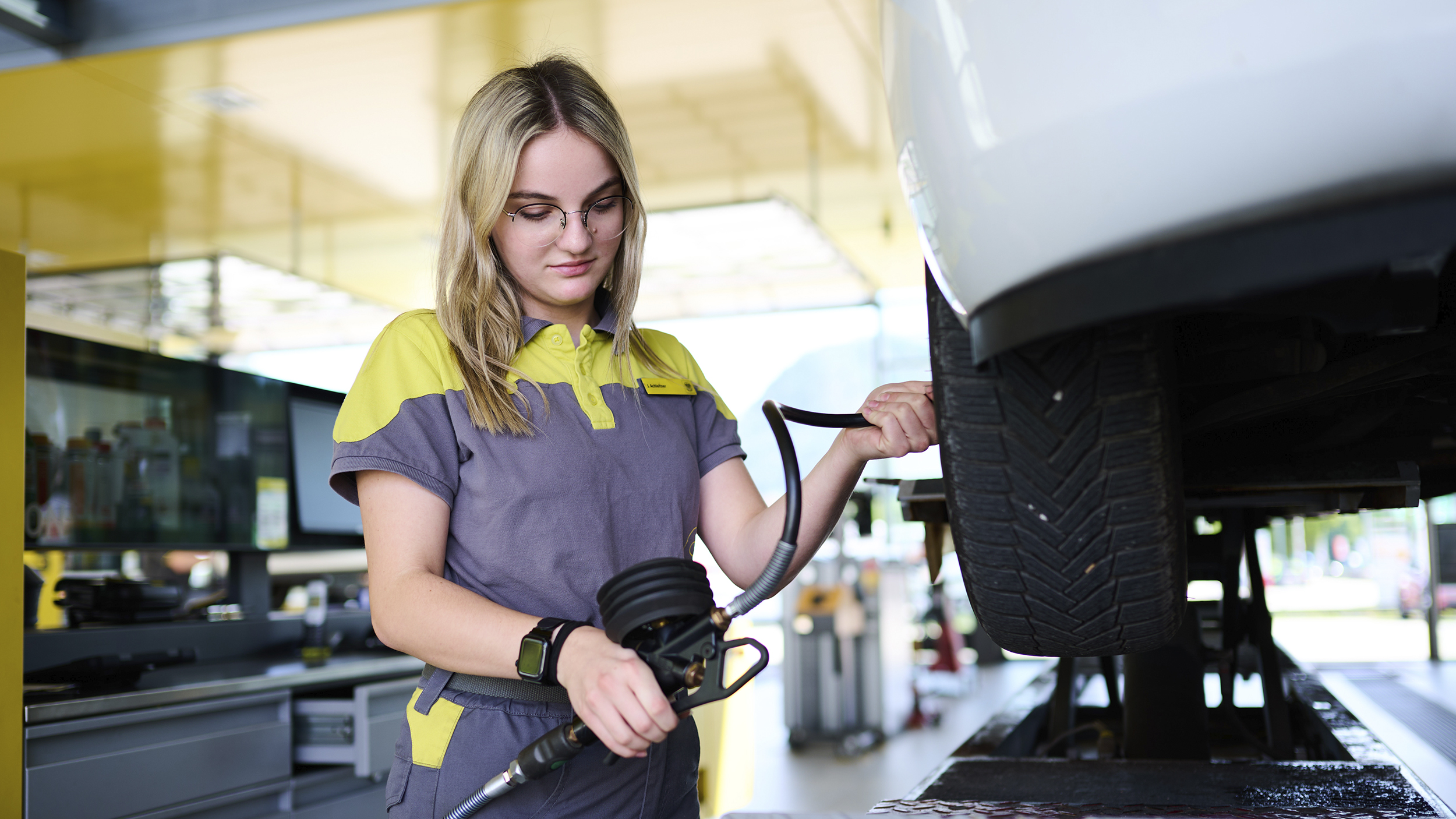 Jessica, ein junger Lehrling in Ausbildung zur Kfz-Technikerin misst den Reifendruck an einem Auto.