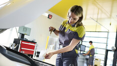 Jessica, ein junger Lehrling in Ausbildung zur Kfz-Technikerin steht vor geöffneter Motorhaube in der ÖAMTC-Werkstatt und kontrolliert den Ölpegel.