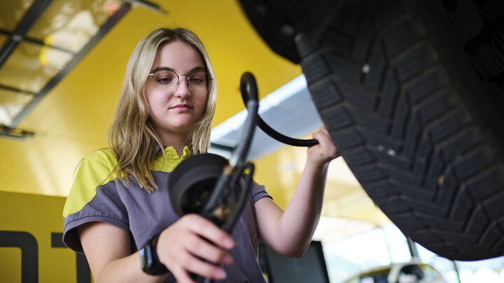 Jessica, ein junger Lehrling in Ausbildung zur Kfz-Technikerin misst den Reifendruck an einem Auto.