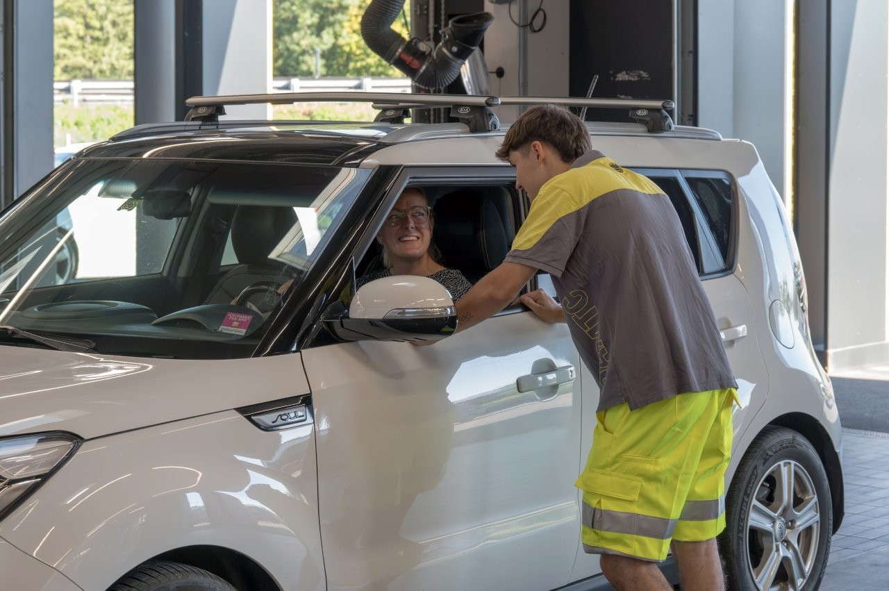 Auf dem Bild sieht man einen jungen Mitarbeiter des ÖAMTC. er spricht durch das geöffnete Seitenfenster eines weißen Autos mit einer Frau.