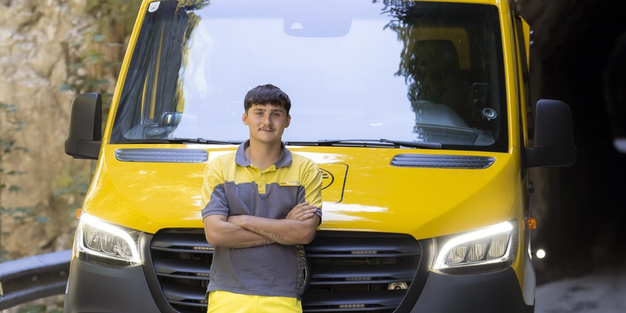 Auf dem Bild sieht man einen jungen ÖAMTC Mitarbeiter. er lehnt mit verschränkten Armen an einen gelben Klein LKW.