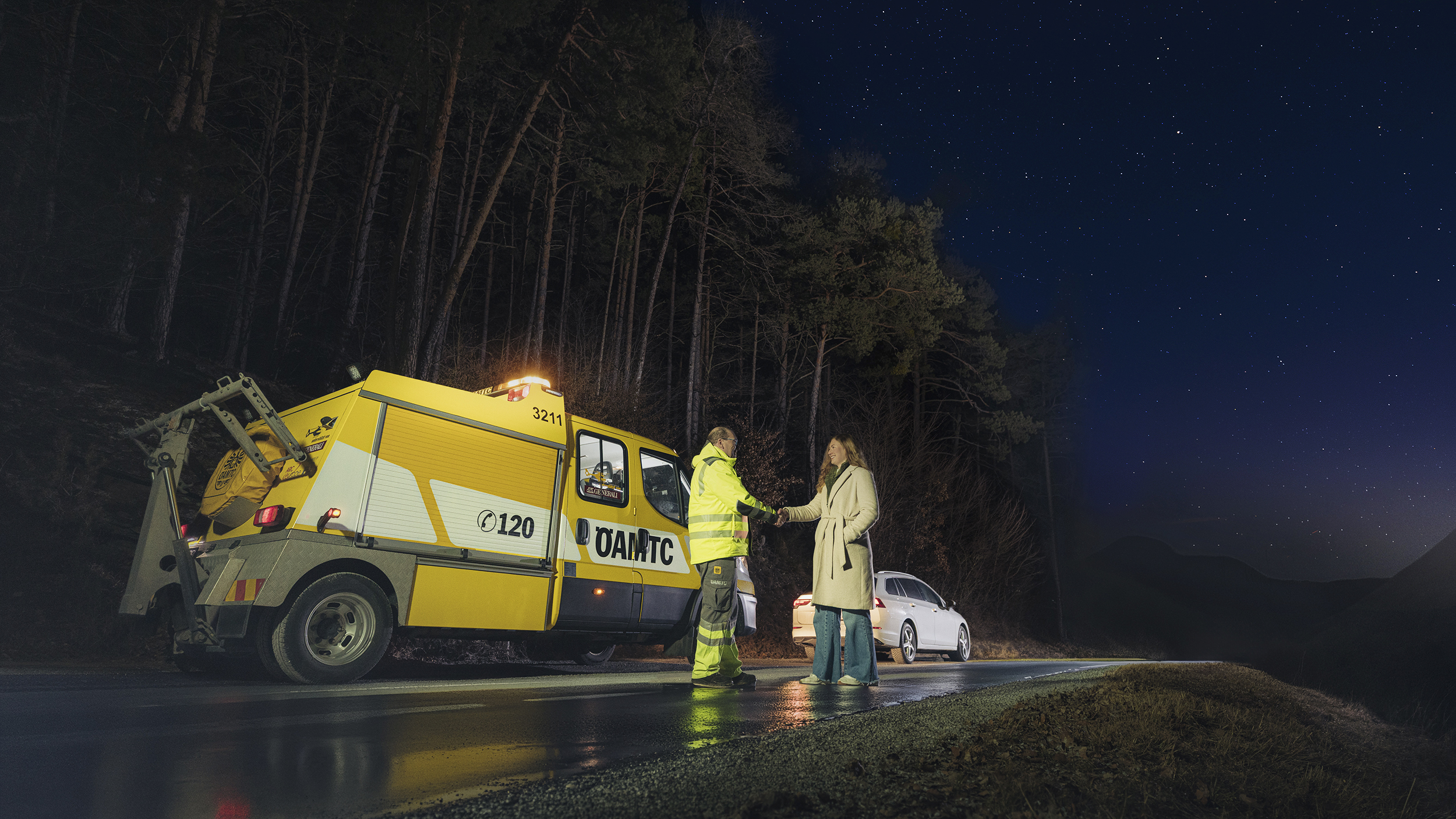 Ein ÖAMTC-Pannenhelfer steht mit einer Frau neben einem Pannenauto auf der Straße. 