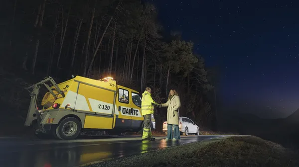 Ein ÖAMTC-Pannenhelfer steht mit einer Frau neben einem Pannenauto auf der Straße.