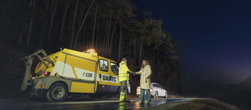 Ein ÖAMTC-Pannenhelfer steht mit einer Frau neben einem Pannenauto auf der Straße.
