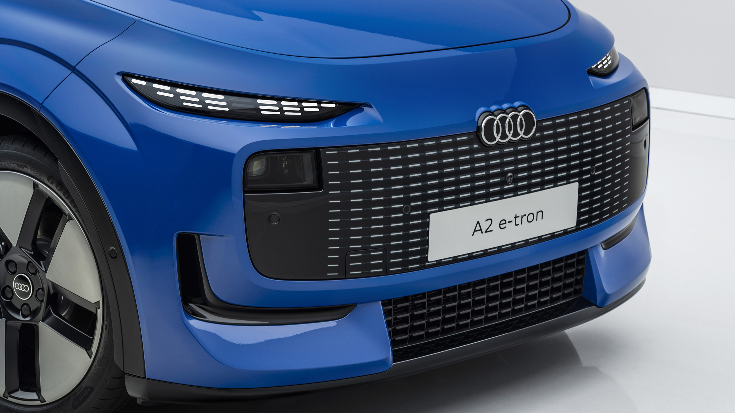Detailaufnahme von Kühlergrill und Scheinwerfer eines blauen Audi A2 e-tron, der in einem weißen Studio steht.