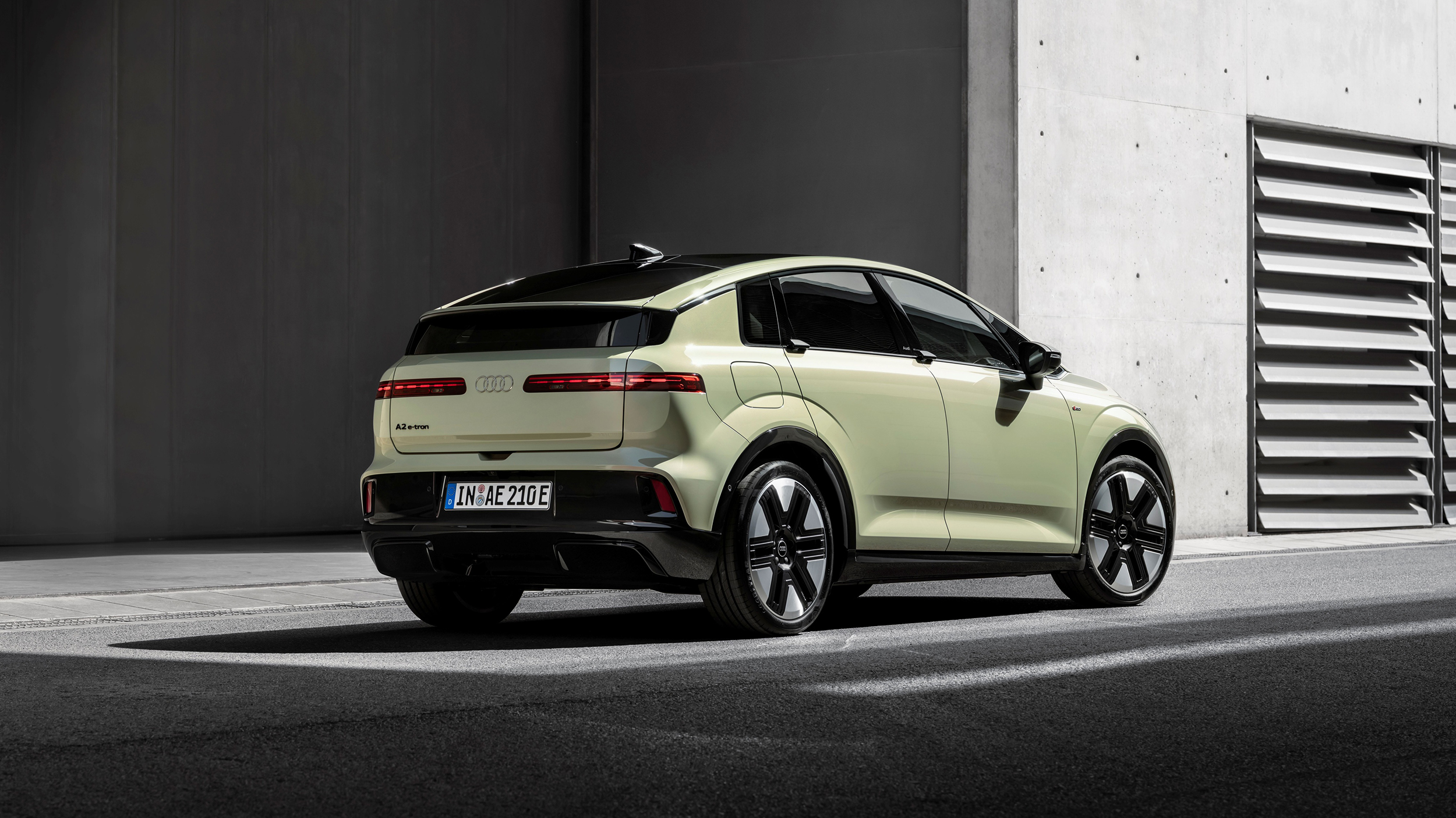 Heck eines gelben Audi A2 e-tron, der vor einem grauen Gebäude aus Beton steht.
