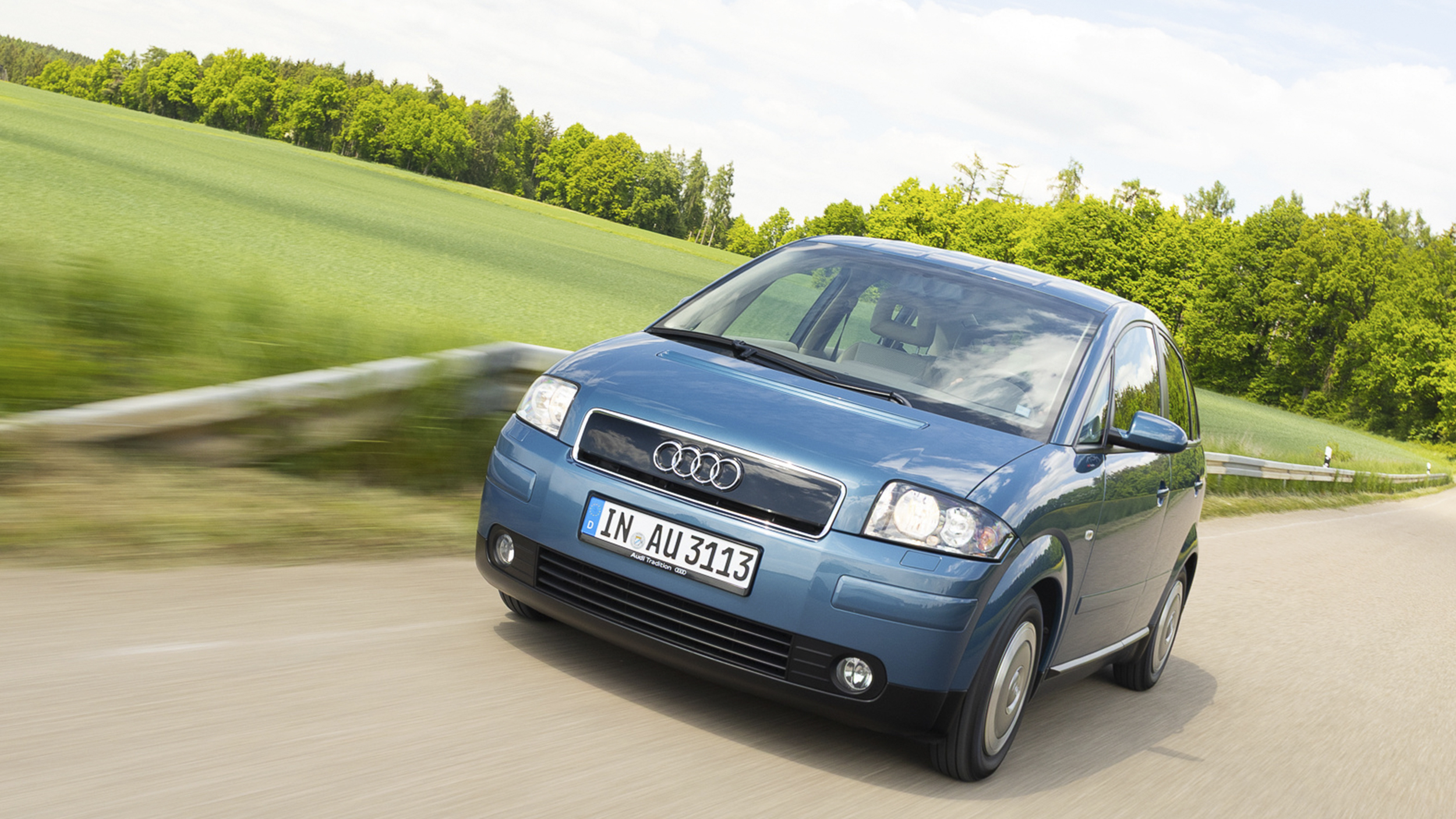 Ein alter, blauer Audi A2 fährt auf einer Landstraße. 