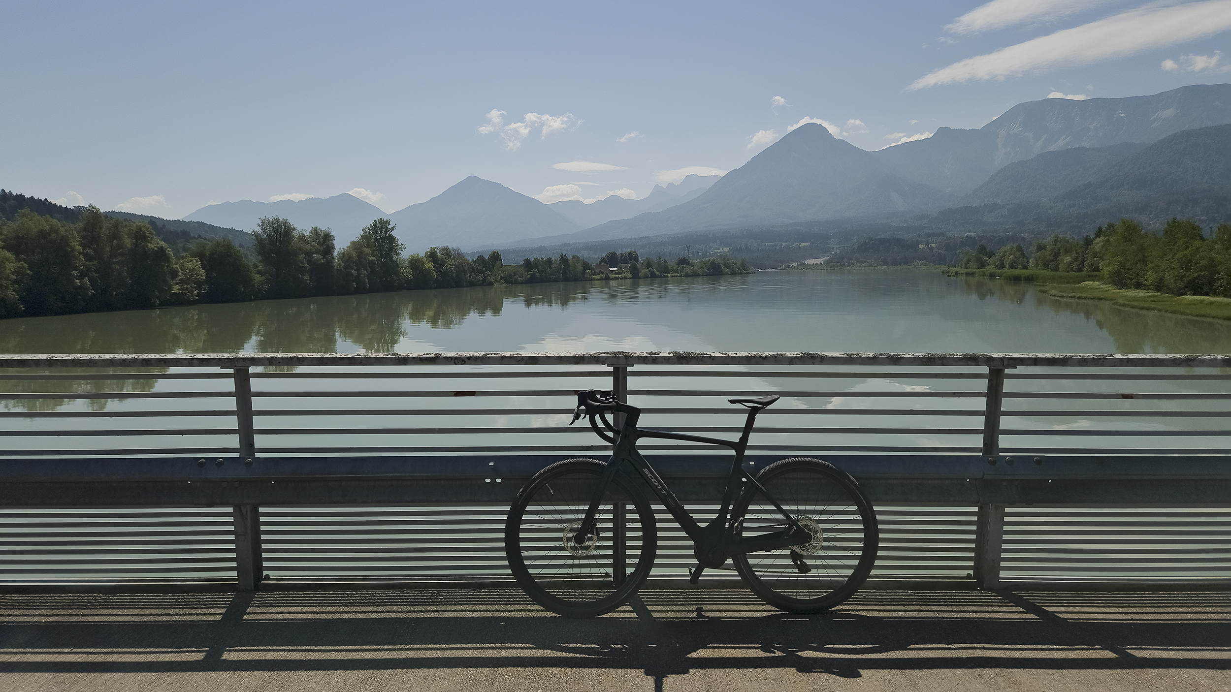 Gravelbike steht angelehnt auf Brückgeländer, im Hintergrund die Drau.