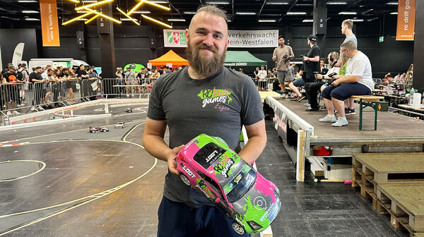 Eugen Netschiporuk mit seinem Nissan Nissan 350 Z. Das Auto ist Neongrün und Neonpink, mit schwarzer Farbe in der Mitte. Darauf ist auch ein gamescom-Aufdruck zu sehen. Eugen trägt ein RC Drift Shirt, er hat einen längeren dichten Bart und die Haare hochgebunden.