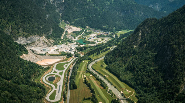 Luftaufnahme der Experience World Saalfelden - man sieht eine asphaltierte Rundstrecke, einen Offroad-Bereich, einen See und Teile eines Golfplatzes, mitten im Tal eines malerischen Alpenpanoramas