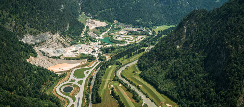 Luftaufnahme der Experience World Saalfelden - man sieht eine asphaltierte Rundstrecke, einen Offroad-Bereich, einen See und Teile eines Golfplatzes, mitten im Tal eines malerischen Alpenpanoramas