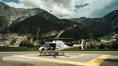 Im Bild ist der Hubschrauber der Experience World Saalfelden zu sehen, auf einem Landeplatz, vor einer malerischen Alpenkulisse