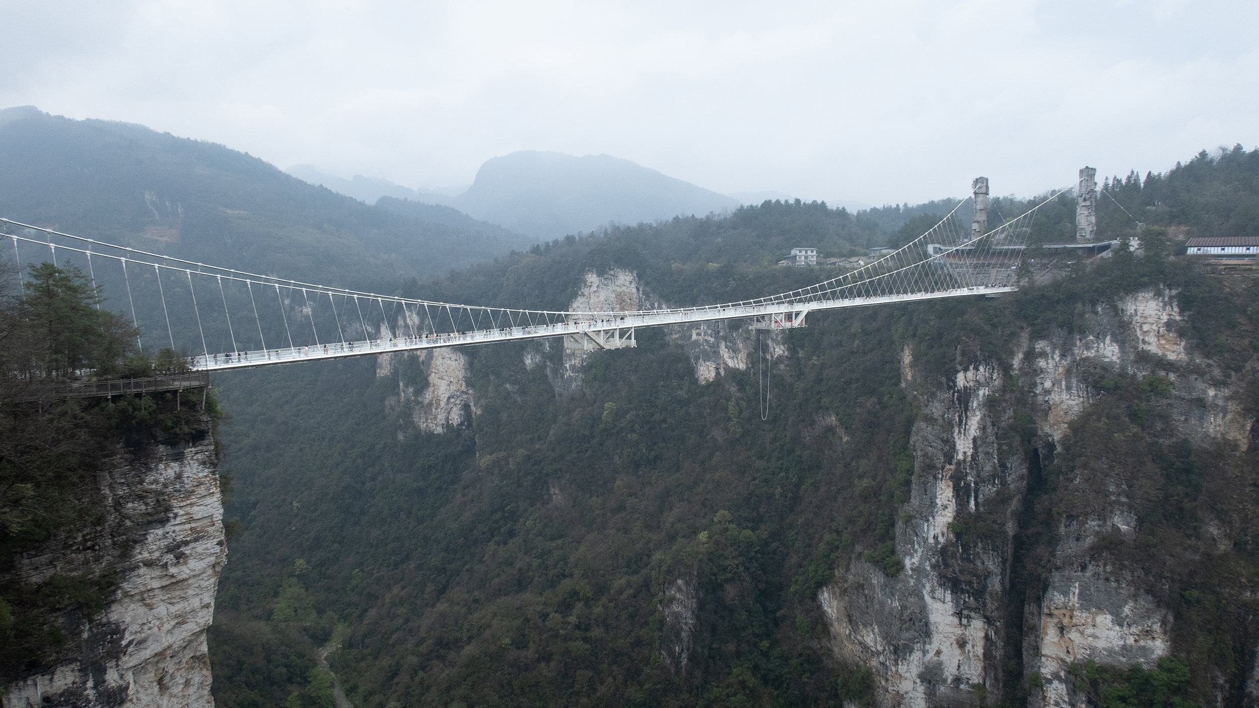Fußgänger-Hängebrücke überspannt eine bewaldete Schlucht zwischen steilen Felswänden.