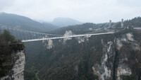 Fußgänger-Hängebrücke überspannt eine bewaldete Schlucht zwischen steilen Felswänden.