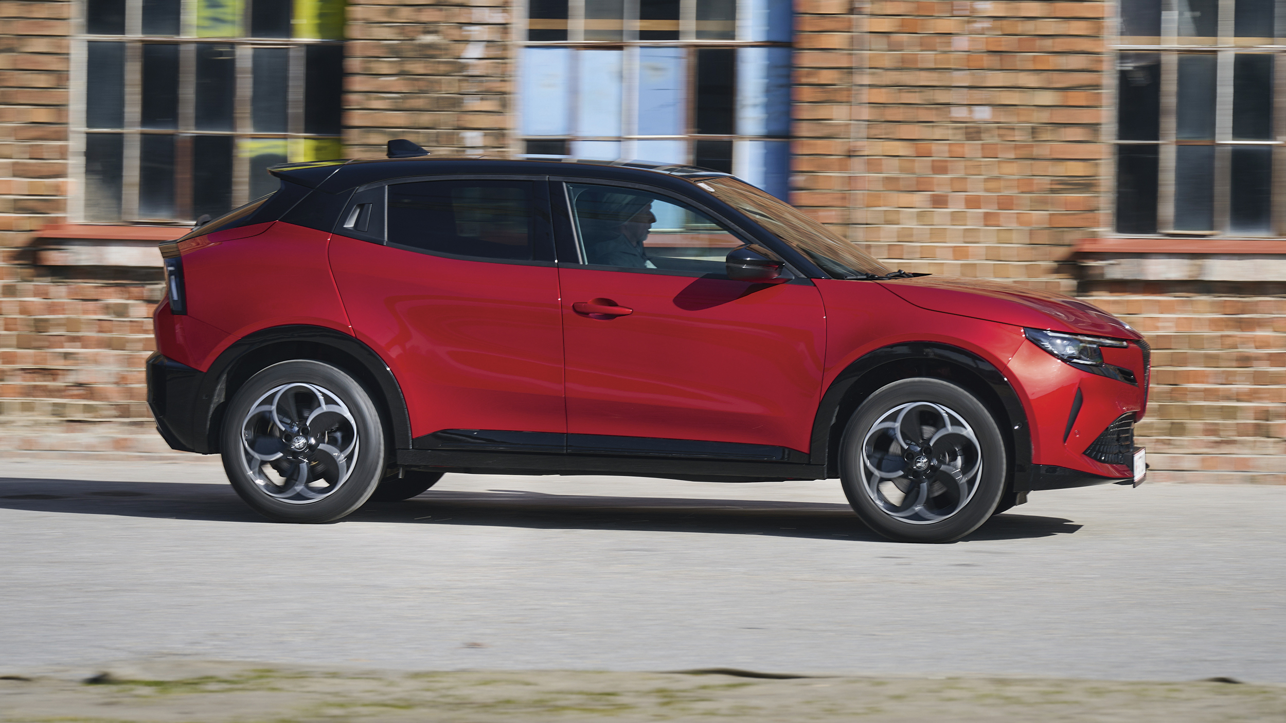 Roter Alfa Romeo Junior Ibrida Q4 fährt von links nach rechts vor einer Backsteinfassade vorbei.