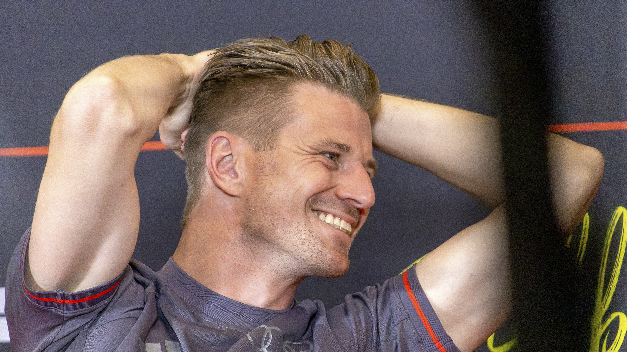 Nico Hülkenberg im grauen Audi-Revolut-Teamshirt lächelt und hält beide Hände hinter dem Kopf.