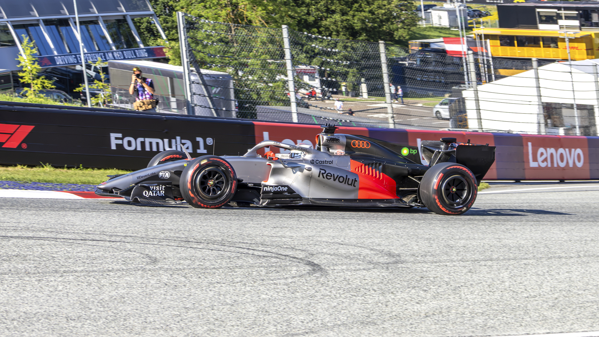 Audi-Formel-1-Rennwagen auf der Strecke vor einer voll besetzten Tribüne und der Red-Bull-Ring-Stierskulptur.