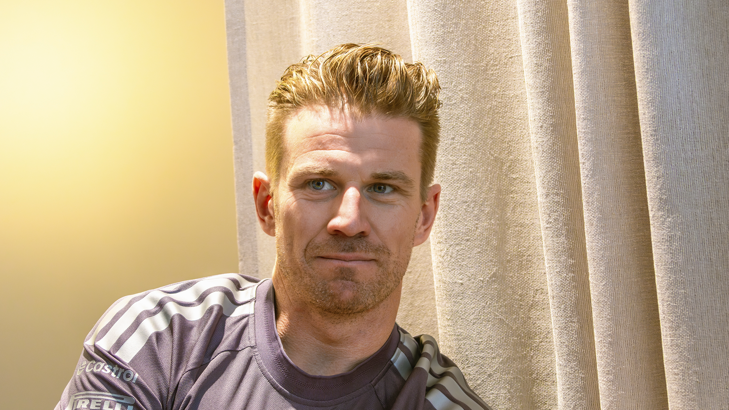 Porträt von Nico Hülkenberg im grauen Audi-Revolut-Teamshirt vor einem hellen Vorhang.