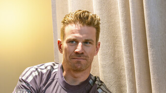 Porträt von Nico Hülkenberg im grauen Audi-Revolut-Teamshirt vor einem hellen Vorhang.