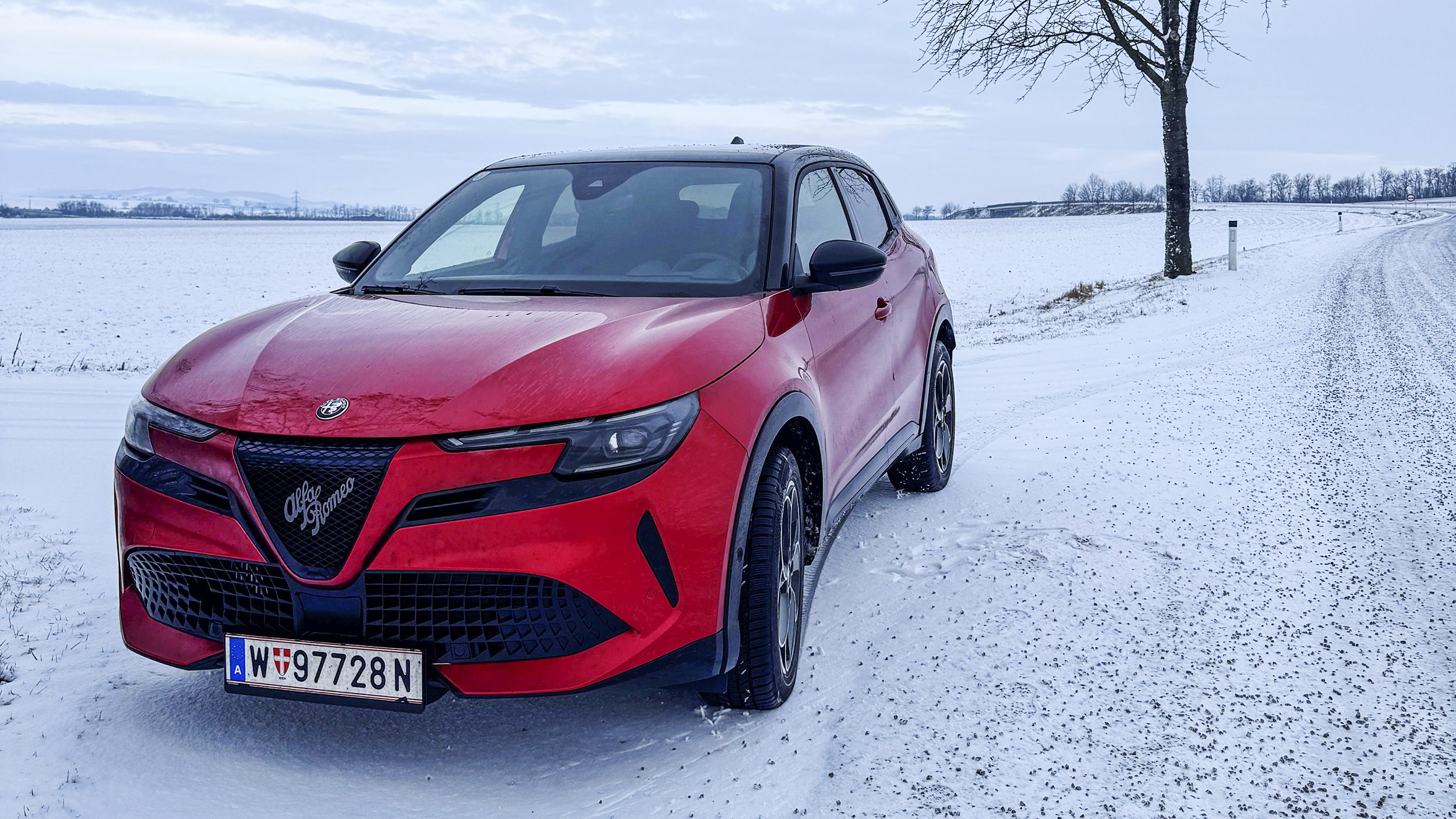 Roter Alfa Romeo Junior im Winter auf verschneiter Landstraße.