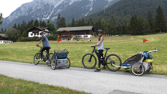 Ein Ehepaar ist mit E-Bike und jeweils einem Kinder-Radanhänger in den Bergen unterwegs.