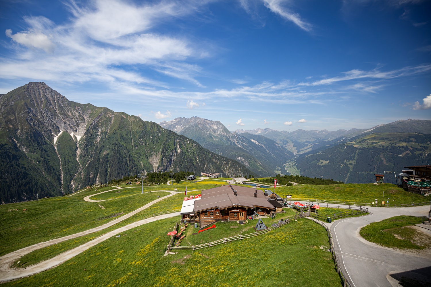 Das Bild zeigt eine grüne Wiese, eine Almhütte und eine Bergkette.