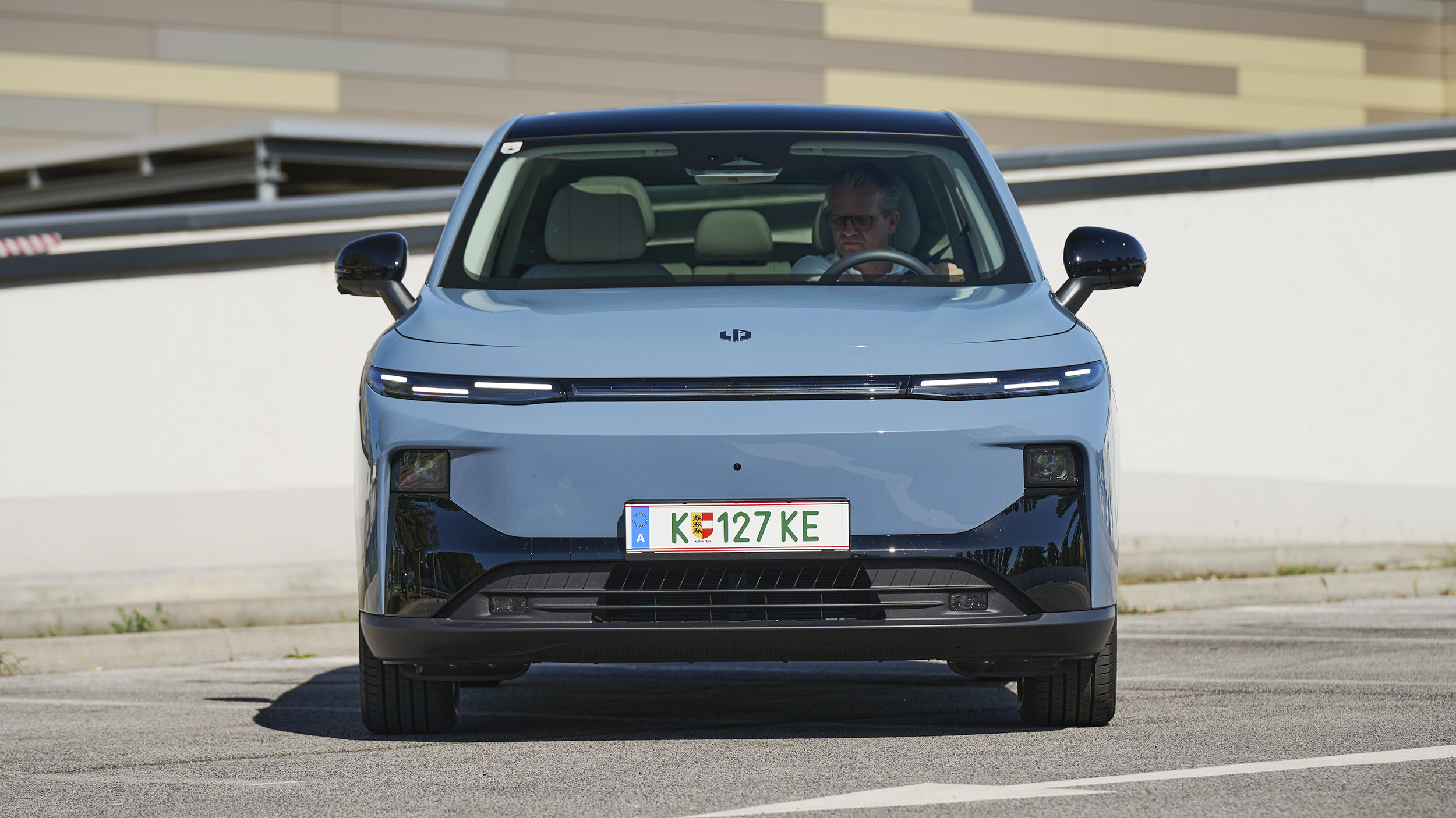 Frontansicht eines hellblauen Leapmotor B10 auf einem Parkplatz; eine Person sitzt am Steuer.