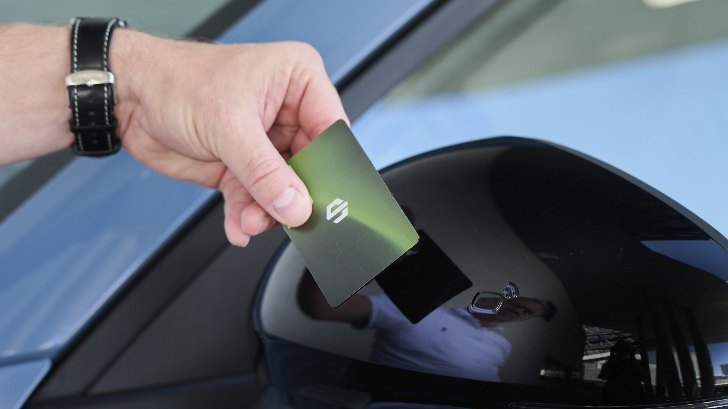 Eine Hand hält eine grün-schwarze Schlüsselkarte vor den schwarzen Sensorbereich am Außenspiegel des Leapmotor B10.