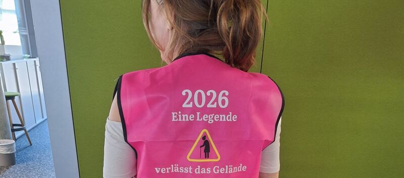 Eine Person steht vor einer grünen Wand. Sie trägt eine rosa warnweste. Auf dieser steht. 2026. Eine Legende verlässt das Gelände