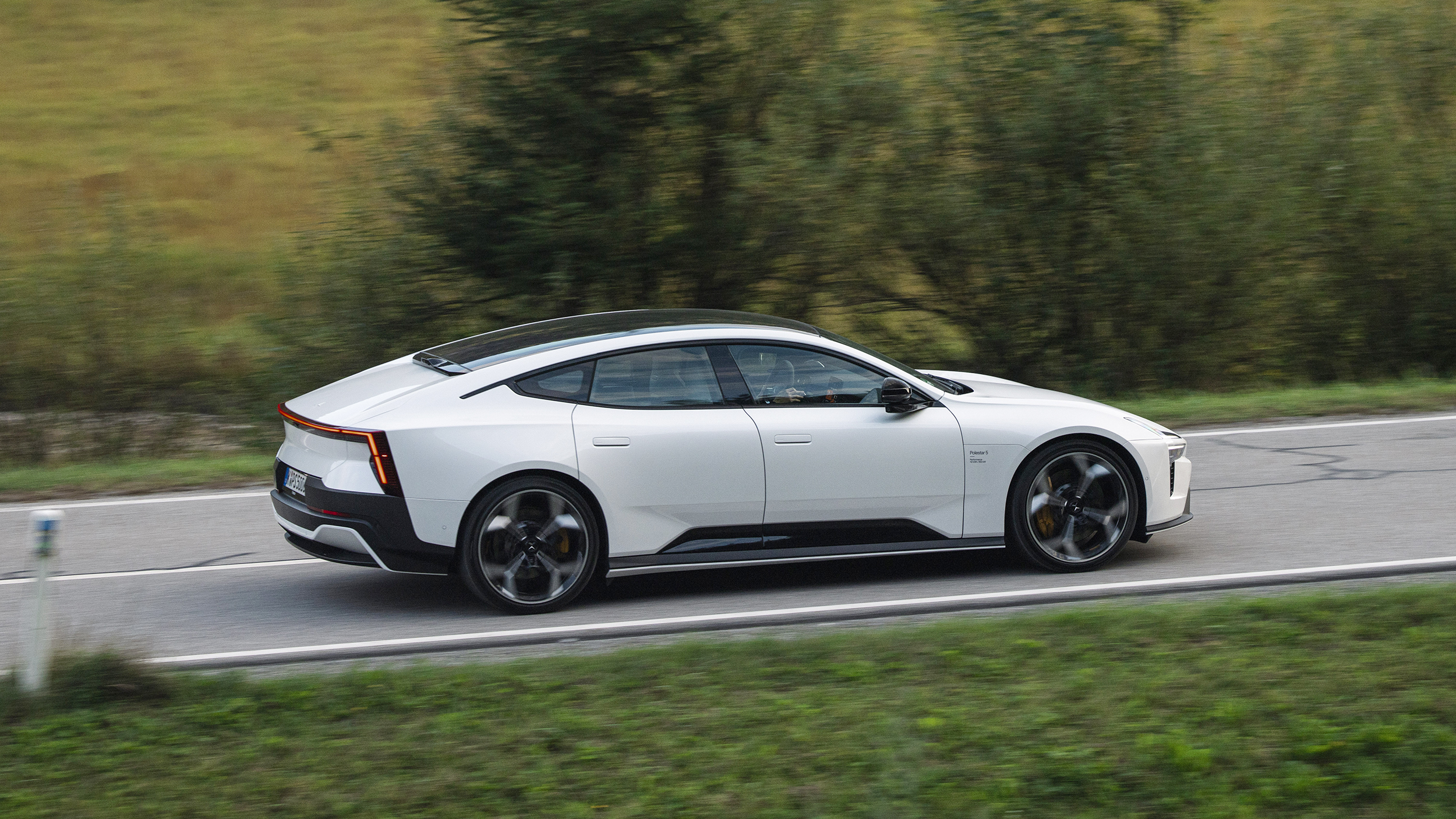 Weißer Polestar 5 in Seitenansicht auf einer Landstraße, der Hintergrund ist durch die Bewegung unscharf.