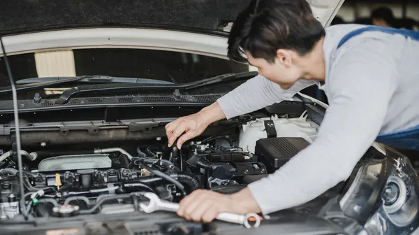 Junger Kfz-Techniker begutachtet das Innere unter der Motorhaube eines Autos.