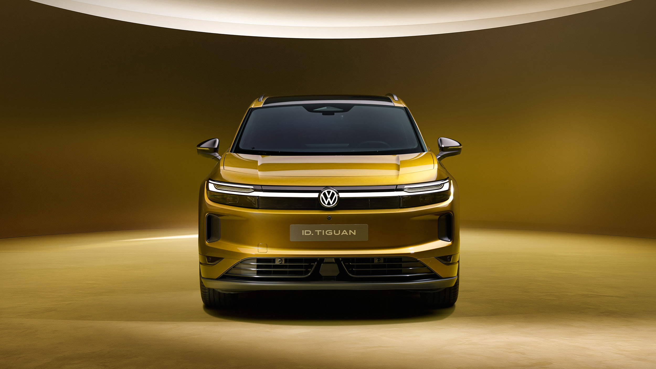 Goldgelber Volkswagen ID. Tiguan in direkter Frontansicht mit durchgehendem LED-Leuchtband und VW-Logo.