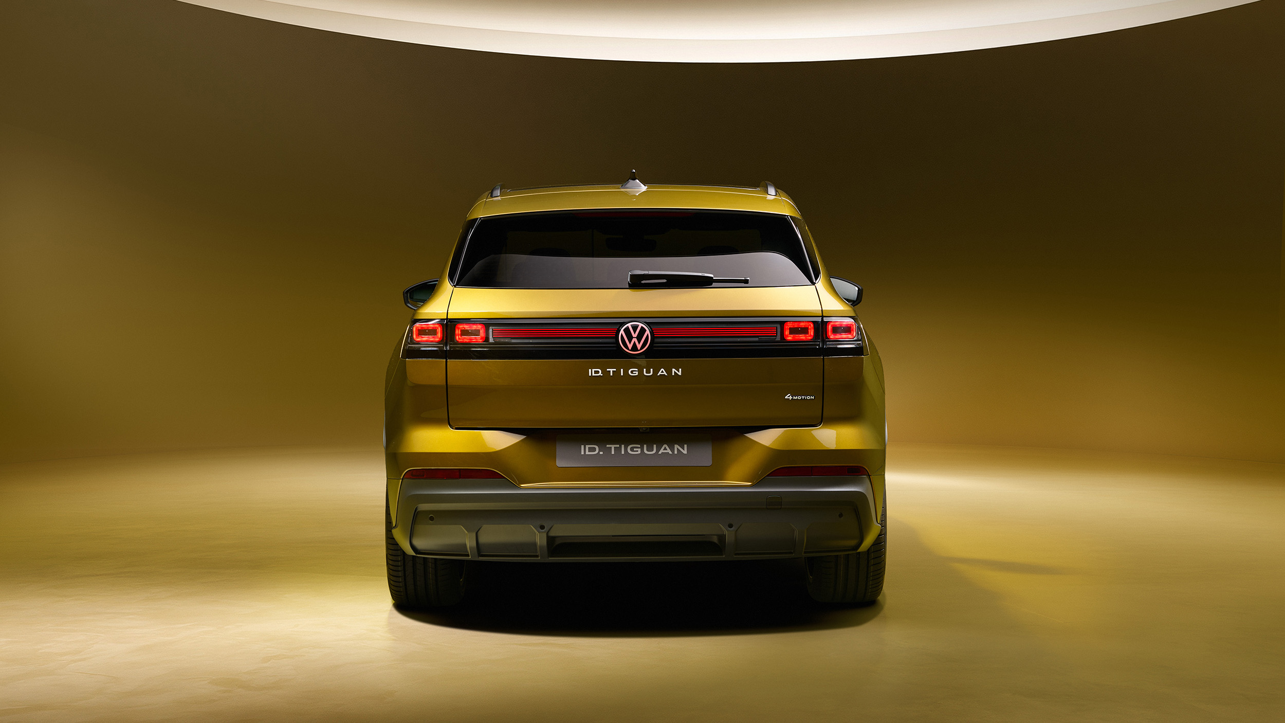 Goldgelber Volkswagen ID. Tiguan in direkter Heckansicht mit leuchtendem roten LED-Band und Modellschriftzug.