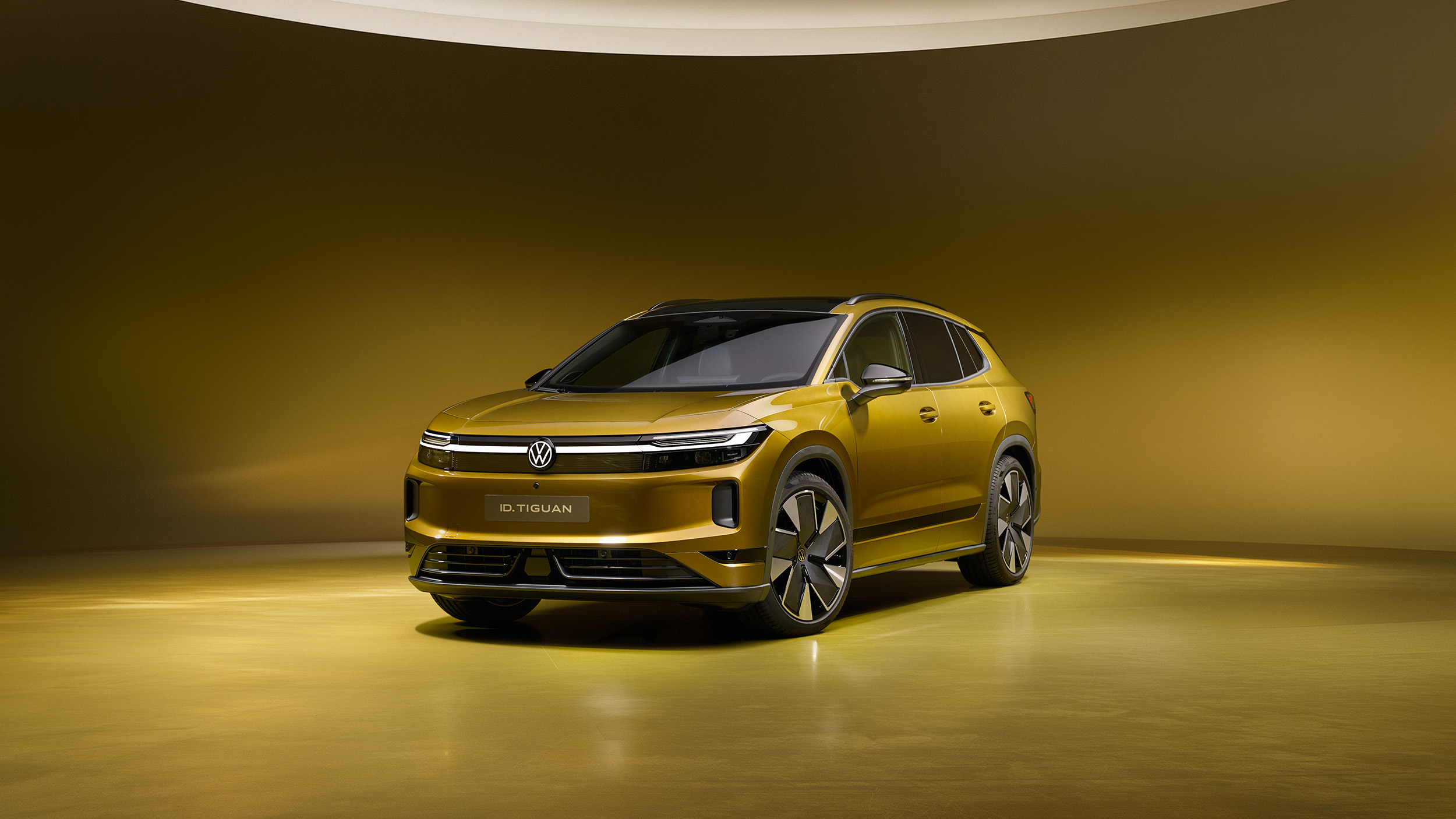 Goldgelber Volkswagen ID. Tiguan in Frontansicht von schräg links in einem gelb beleuchteten Studio.